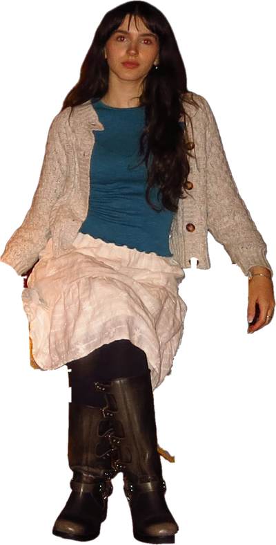 A person in a cream cable-knit cardigan, teal top, long white skirt and buckled brown boots